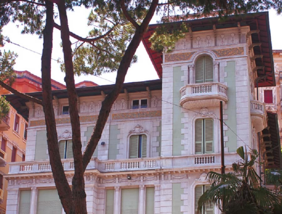 Edificio storico in stile Liberty con balconi, finestre e decorazioni elaborate, alberi in primo piano, architettura italiana.